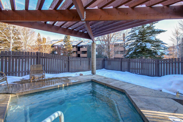 Soak in the steaming hot tub beneath a rustic timber pergola, surrounded by snow-dusted trees and crisp mountain air—a perfect winter escape to unwind and warm up.