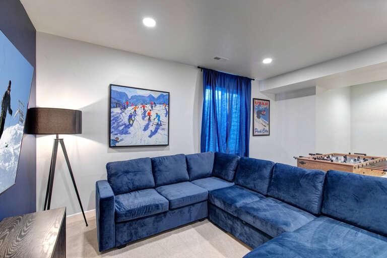 A cozy entertainment space awaits with plush blue sectional seating, foosball fun, and ski-themed art setting the perfect après-ski mood.