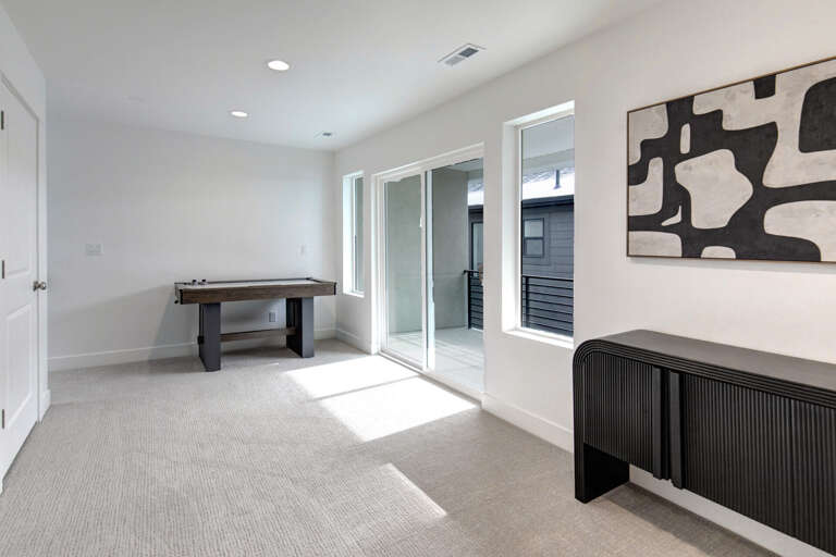 Your own game room awaits, complete with an air hockey table and sleek modern furnishings, flooded with natural light from floor-to-ceiling windows leading to your private balcony.