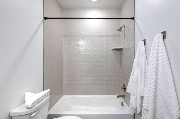 Step into a spotless modern bathroom with sleek tiled walls, a refreshing rainfall shower, and plush towels ready for your ultimate relaxation.