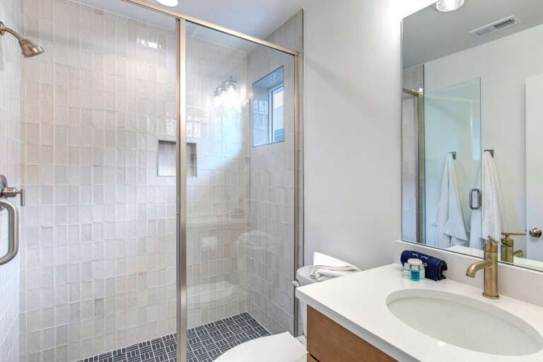 A bright, modern bathroom awaits you with a spacious glass-enclosed shower, elegant tile work, and fresh linens ready for your stay.