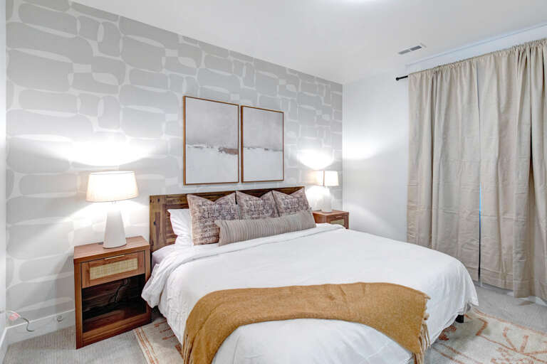 Sink into plush bedding beneath soft lamplight and elegant artwork. Your serene retreat features warm wood accents and soothing neutral tones for complete relaxation.
