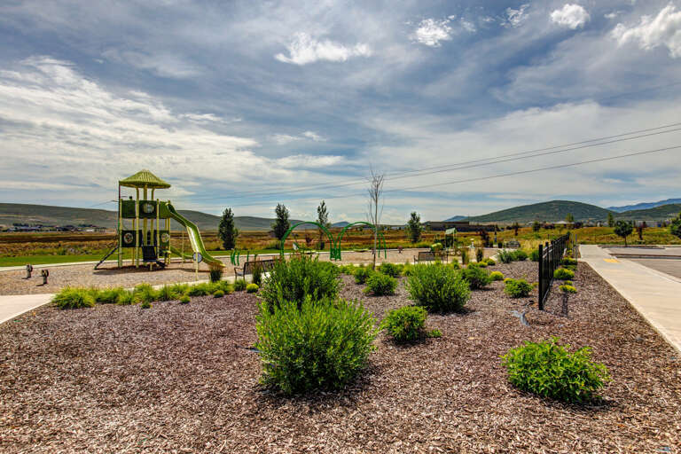 A landscaped neighborhood park with playground equipment, mountain views, and open green spaces welcomes families in the surrounding community.