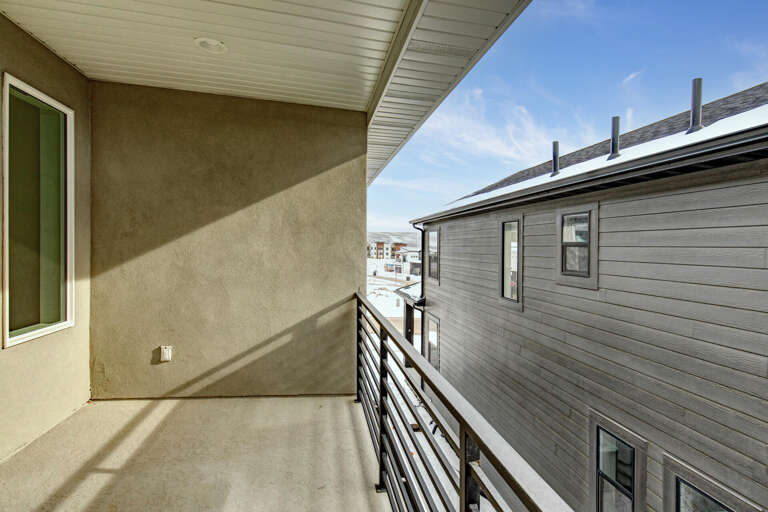 A covered balcony with modern railing provides a private outdoor retreat. Blue skies and clean lines create a bright, airy escape just steps from your door.