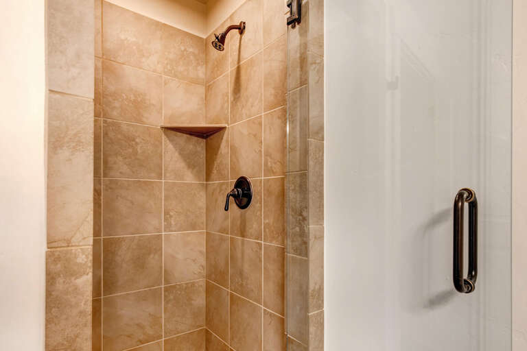 Step into your spa-like walk-in shower with elegant tiled walls, bronze fixtures, and a built-in corner shelf for your toiletries.