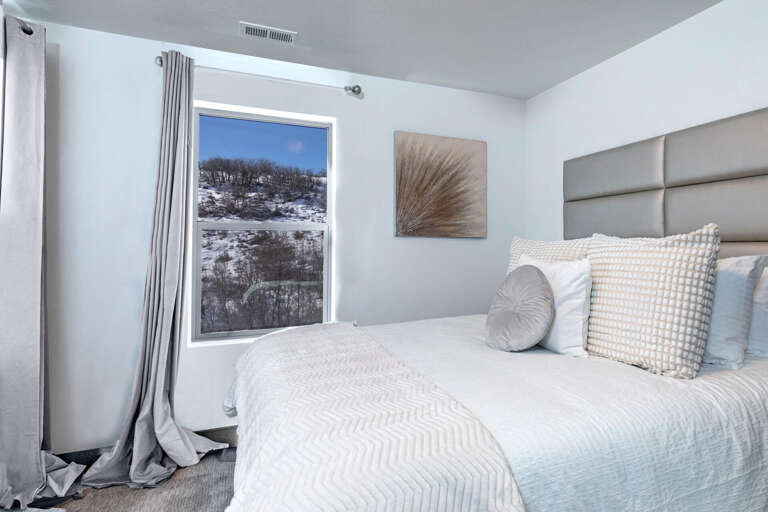 Drift off in this serene bedroom where crisp linens and plush pillows promise restful nights. Wake to stunning snowy hillside views framed by your window—a tranquil winter escape.