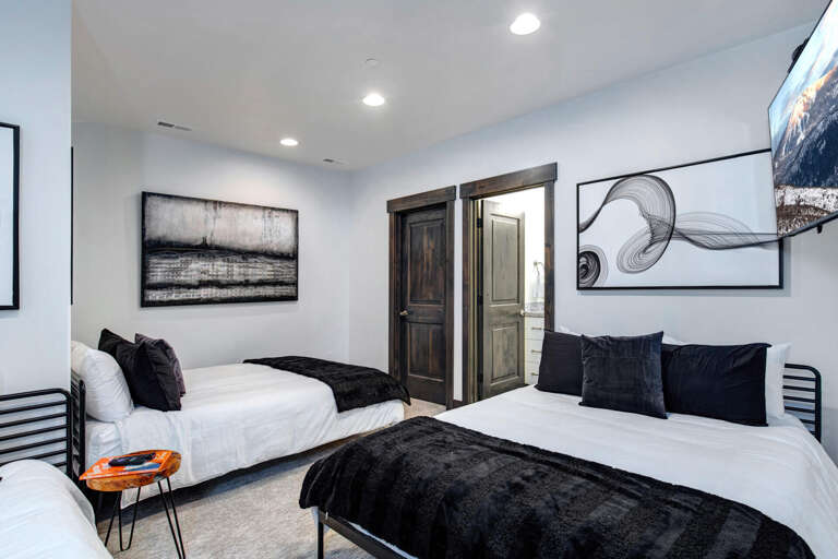 Sink into plush white bedding topped with velvety black throws in this modern twin bedroom. Curated artwork and warm lighting create your serene retreat for restful nights.