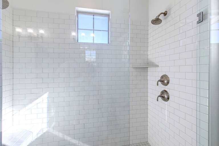 Step into your pristine walk-in shower with classic subway tile, dual fixtures for customized comfort, and a built-in bench perfect for unwinding under the rainfall showerhead.