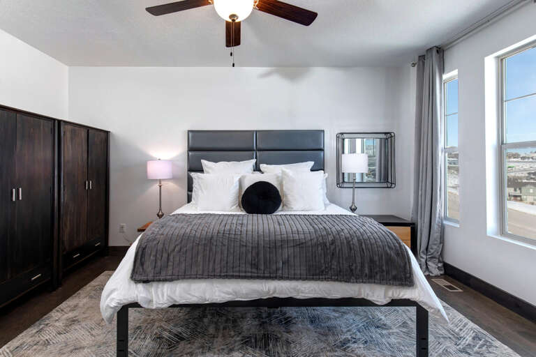 Sink into the plush bedding beneath a gentle ceiling fan as natural light pours through your windows, highlighting the sleek furniture and calming gray tones of your personal retreat.