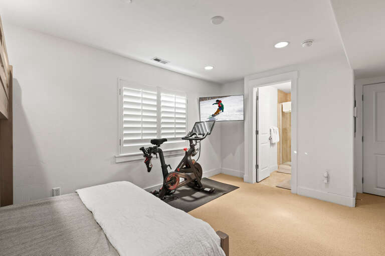 Your private bedroom features a workout area with a stationary bike, wall-mounted TV for entertainment, and en-suite bathroom access—perfect for staying active during your stay.