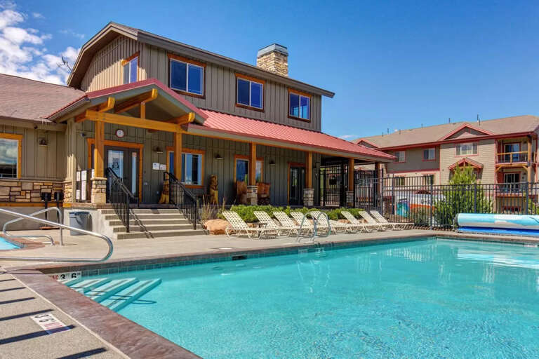 The outdoor pool area features loungers arranged poolside, with the main property building and adjacent structures framing the sunny communal space.