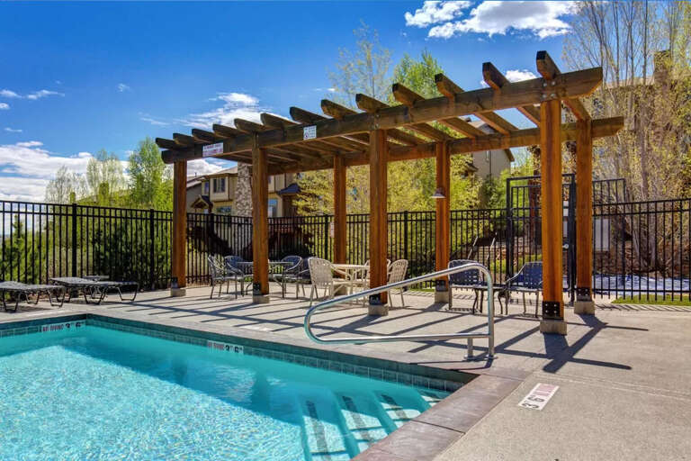 The property features an outdoor pool area with a pergola-covered deck, lounge seating, and mountain views surrounded by trees and landscaping.