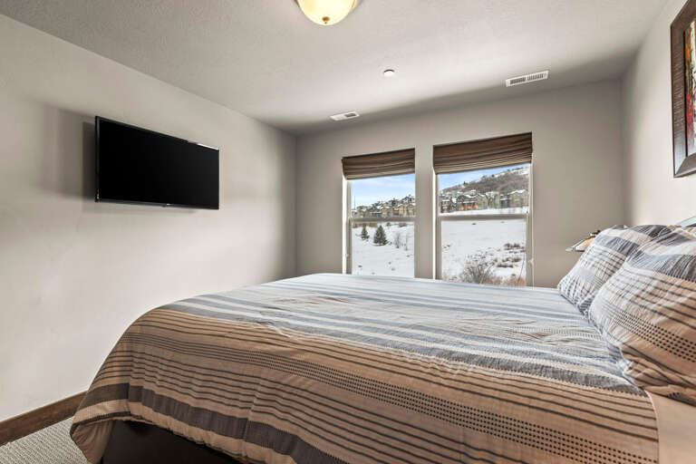 Winter mountain slopes frame your windows, while plush bedding and a wall-mounted TV create your cozy retreat after a day on the hills.