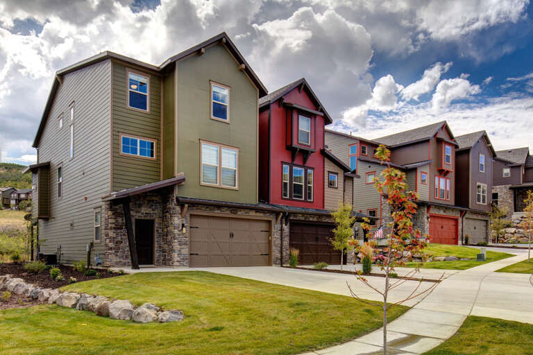 Colorful townhomes set within a peaceful neighborhood, framed by manicured lawns and mountain views beneath dramatic clouds.