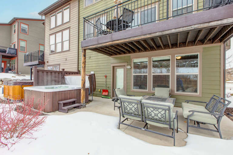 Multi-level rental property featuring a private hot tub, covered patio with seating, and upper balcony in a mountain neighborhood setting.