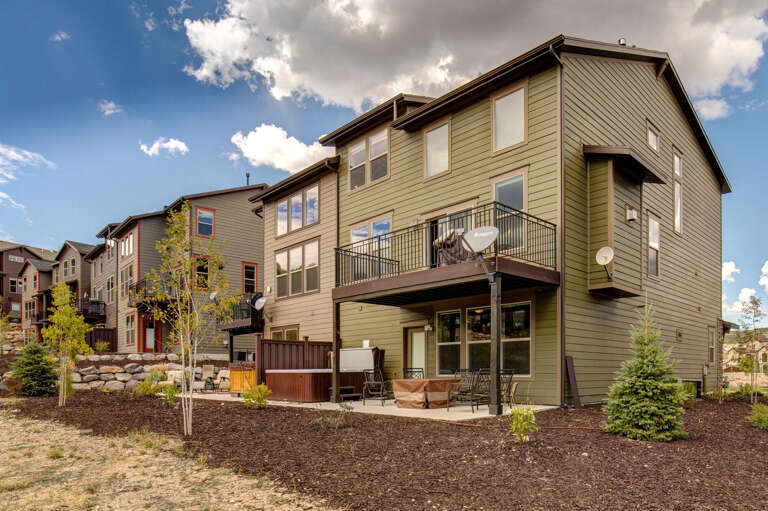 Mountain-style vacation rental featuring a private hot tub and spacious balcony, surrounded by landscaped grounds with young trees and natural mulch, located in a peaceful residential neighborhood.