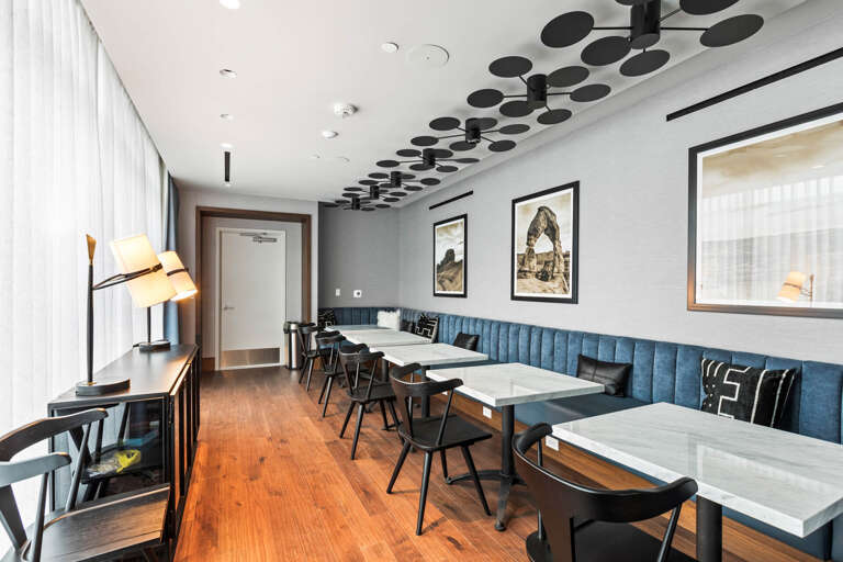 A stylish dining space featuring marble-topped tables, plush navy banquette seating, and striking sculptural ceiling details. Warm wood floors and modern artwork create an inviting atmosphere for your meals.