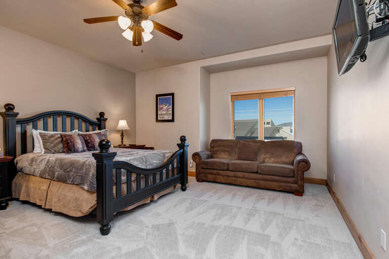 Rest comfortably in your spacious bedroom featuring a cozy leather loveseat, ceiling fan, and natural light streaming through large windows.