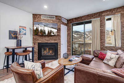 Cozy up by the fireplace with mountain views stretching beyond your windows, featuring rich leather seating and rustic stone accents.