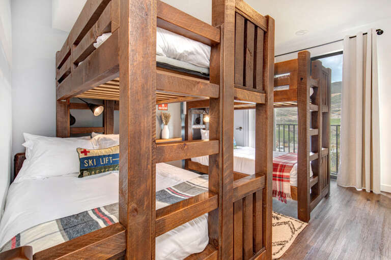 Cozy bunk room with rustic wood frames and crisp linens, perfect for family gatherings. Each bed has its own reading light, and mountain views await through the window.