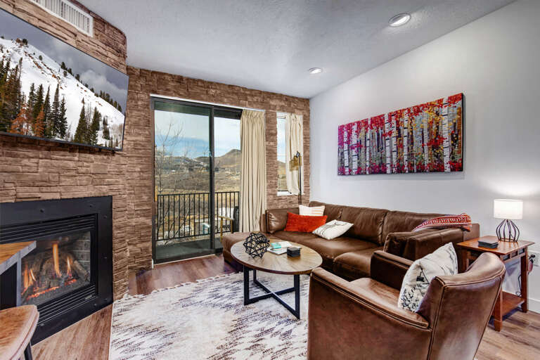 Unwind in your cozy living space with rich leather seating, crackling fireplace, and stunning mountain views through floor-to-ceiling windows.