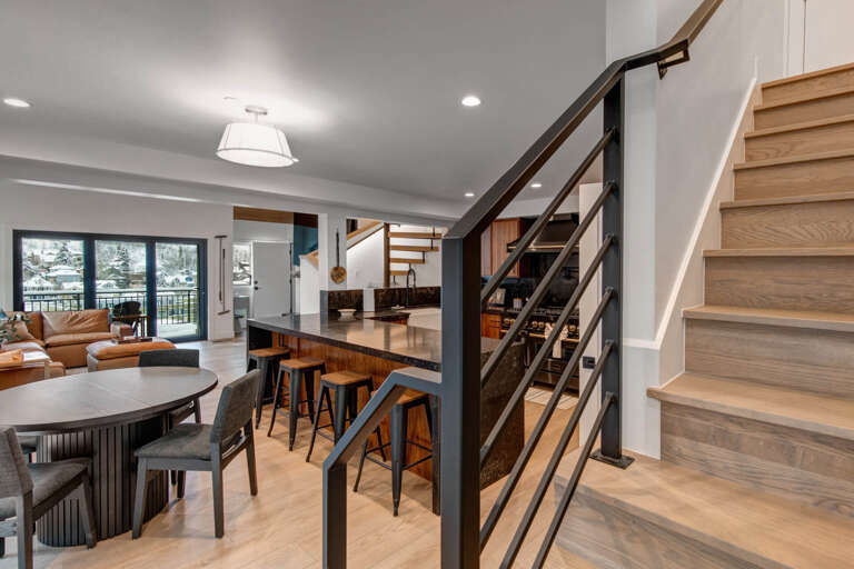 Step into your modern mountain retreat where sleek kitchen island meets warm wood stairs, perfect for gathering after adventures.