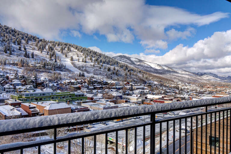 Stunning mountain town vista with snow-covered peaks and charming alpine village below from private balcony.