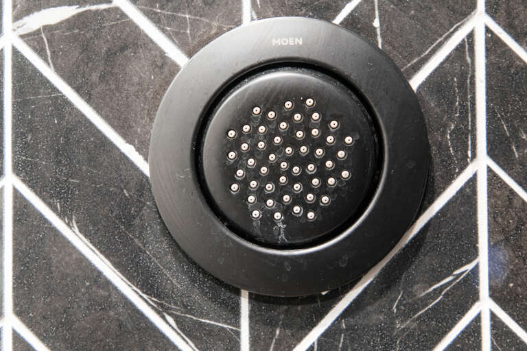 Stylish black drain cover against modern geometric tile creates a sleek, contemporary bathroom detail. Quality fixtures and thoughtful design combine for your refreshing shower experience.