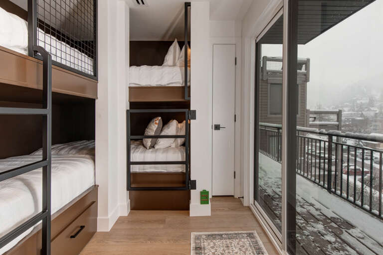 Cozy bunk rooms offer efficient sleeping arrangements with stylish modern design, while your private balcony opens to peaceful winter mountain views, creating a perfect blend of communal comfort and scenic retreat.