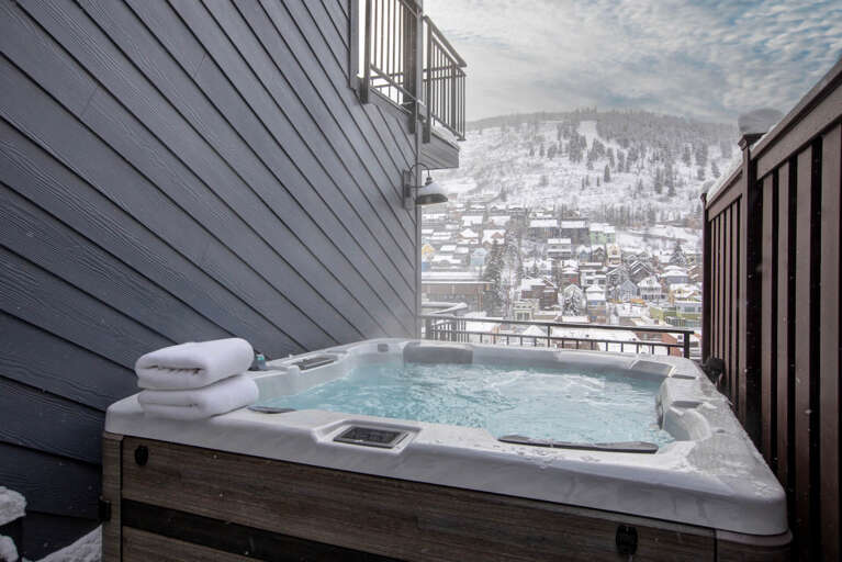Relax in your private hot tub on the terrace, surrounded by a stunning winter alpine village nestled beneath snow-covered mountain slopes, perfect for après-ski unwinding.