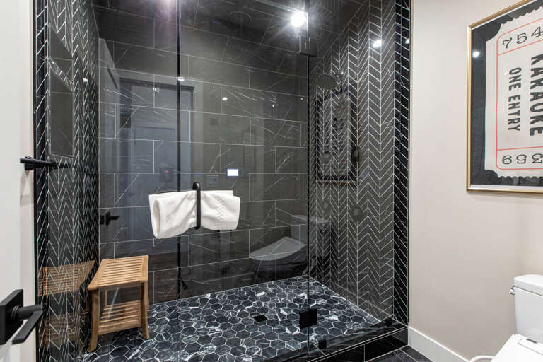 Step into your private spa retreat with a stunning glass-enclosed shower adorned with modern herringbone tiles, complete with a teak bench and plush towels waiting for your relaxation.