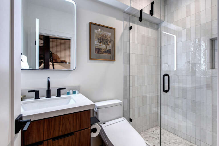 Step into a sleek, modern bathroom with soft lighting, clean lines, and a spacious glass-enclosed shower. Your refreshing retreat awaits—complete with warm wood tones and elegant fixtures.