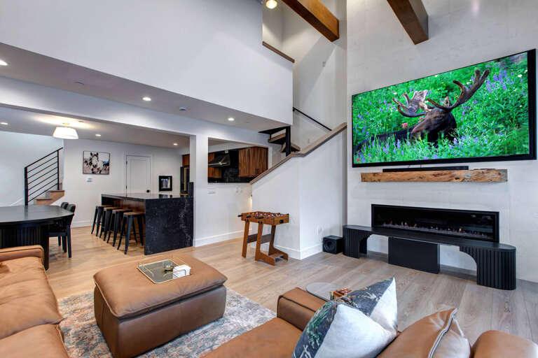 Upper Main 303 Living Room: Relax in your modern living space with soaring beamed ceilings, where your cozy leather seating faces an elegant fireplace and oversized TV.