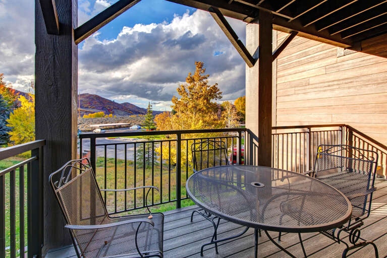 This covered balcony offers stunning mountain views framed by vibrant autumn foliage. Relax at the outdoor table while taking in the dramatic sky and colorful landscape surrounding the property.