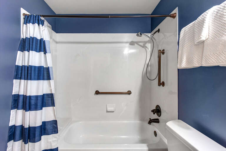 Your nautical-themed bathroom features a pristine tub-shower combo with accessibility grab bars, handheld showerhead, and crisp white towels ready for your arrival.