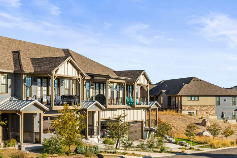 A community of modern mountain homes nestled in a scenic neighborhood, showcasing contemporary architecture with timber accents and spacious decks against a backdrop of natural terrain.