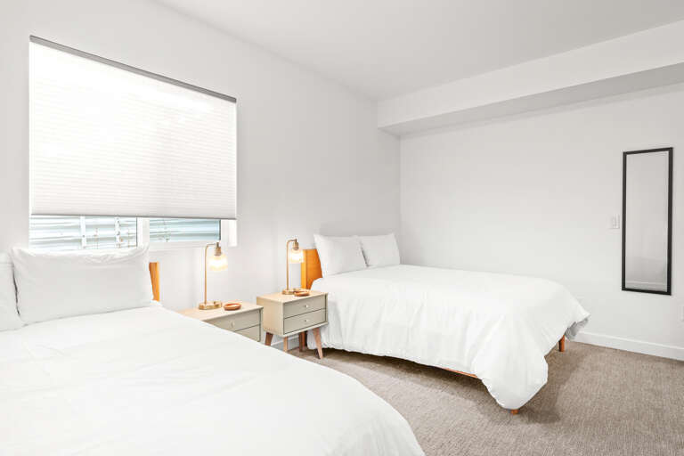 Drift off in crisp white linens as natural light fills your serene bedroom. Two comfortable beds, stylish lamps, and calming décor create your perfect coastal retreat.