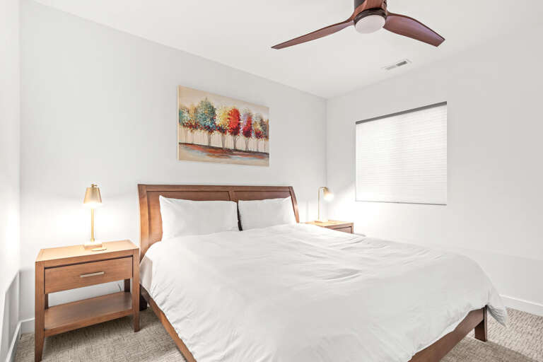 Drift off in crisp white linens under a modern ceiling fan. Natural light filters through your window, while bedside lamps offer a warm glow for evening reading.