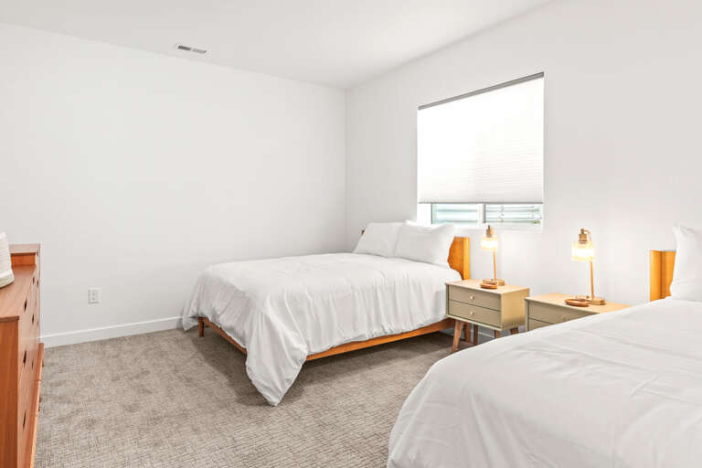 Your tranquil retreat awaits—two cozy beds dressed in crisp linens, warm bedside lighting, and gentle natural light for peaceful mornings and restful nights.