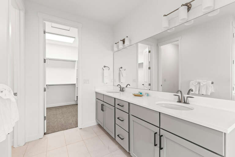 Your private ensuite features dual vanities with modern gray cabinetry and crisp white countertops, offering plenty of space for your morning routine in this bright, inviting bathroom.