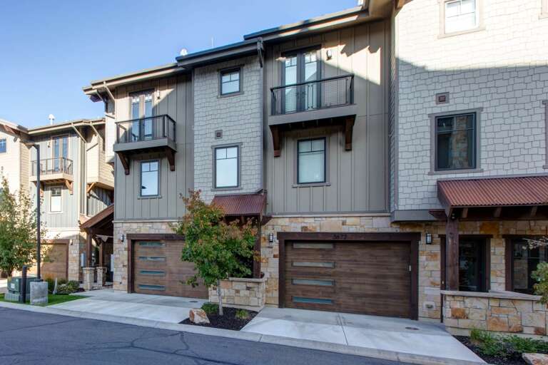 Modern townhomes featuring sleek architecture with private balconies, metal railings, and attached garages situated in a quiet, landscaped residential community.