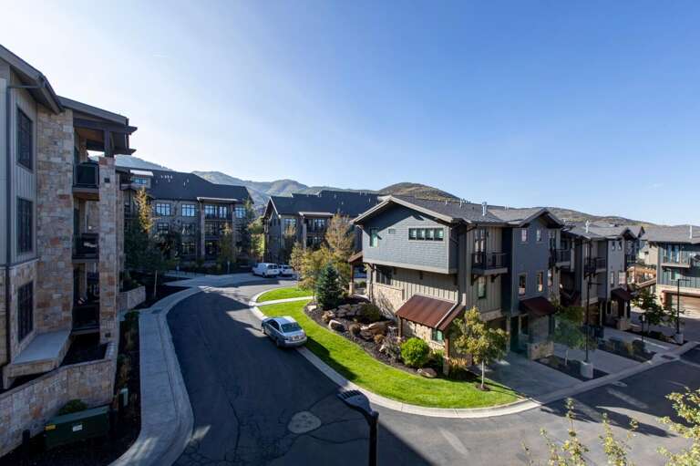 Elegant mountain community featuring modern townhomes and condos with stone and timber accents, set along quiet residential streets with manicured lawns and mature trees.