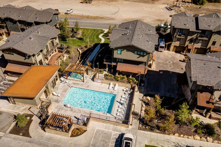 Aerial view of a residential vacation property featuring a large shared pool and hot tub, surrounded by modern townhomes in a mountain resort community.