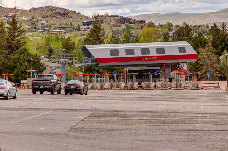 This mountain village features a distinctive cabriolet-style lift station surrounded by forested hillsides and residential neighborhoods, marking the gateway to alpine adventures.