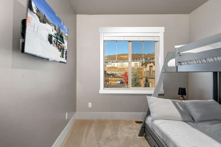 Relax in this cozy bedroom with bunk beds and a large flat-screen TV. The bright window frames neighborhood views, and soft neutral tones create a welcoming atmosphere for restful sleep.