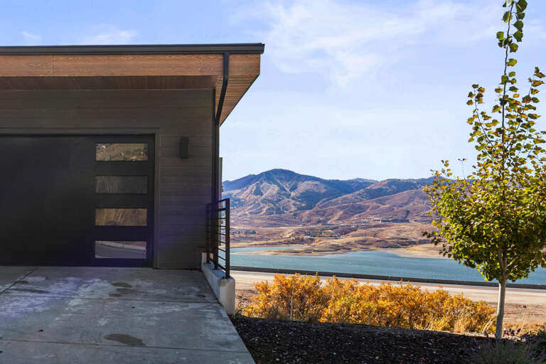 Modern vacation rental entrance with stunning lake and mountain backdrop. The property sits in a scenic natural setting with autumn foliage and expansive western views.