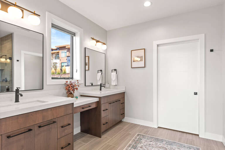 Step into your bright, modern bathroom with dual vanities, warm wood cabinetry, and natural light streaming through the window. Fresh linens and thoughtful design details make your daily routine feel like a retreat.