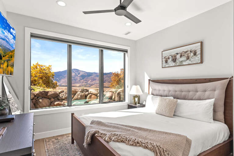 Unwind in your serene bedroom where crisp white linens meet mountain views. The ceiling fan keeps you comfortable while natural light highlights every thoughtful detail designed for your restful escape.