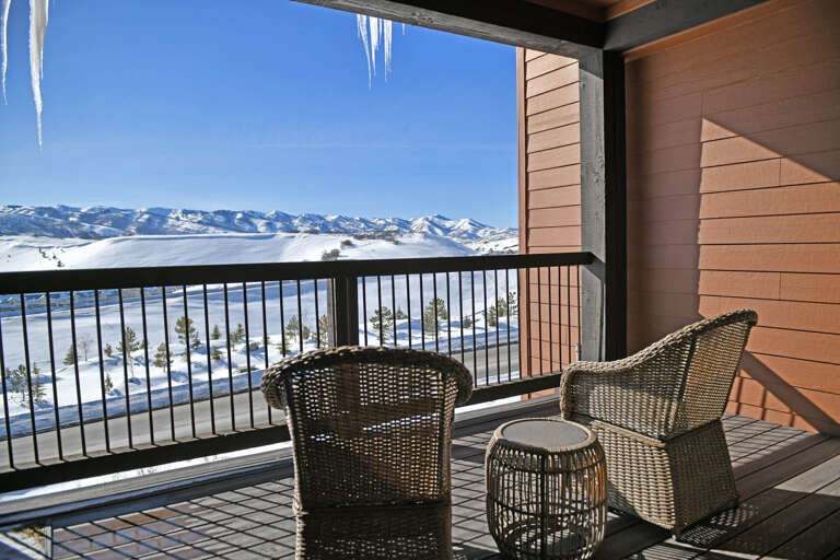 Spectacular snow-covered mountain range and winter landscape visible from this private balcony. Two cozy wicker chairs offer front-row seating to pristine valley views.