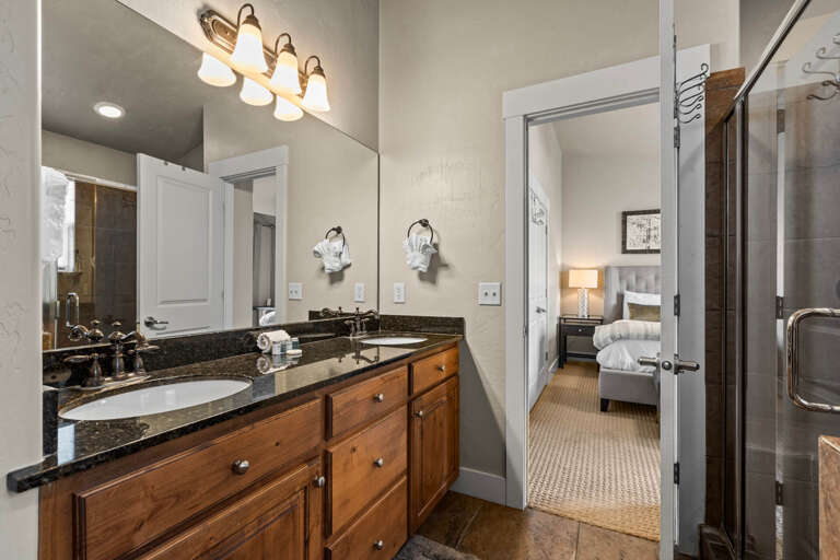 Your private ensuite bathroom features elegant granite counters, warm wood cabinetry, and a spacious walk-in shower—everything you need to refresh before your next mountain adventure.